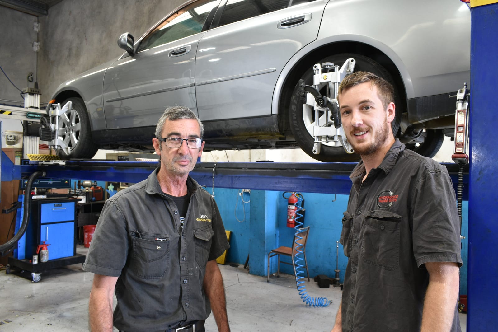 Two Guys Garage mechanics beside a car on a lift