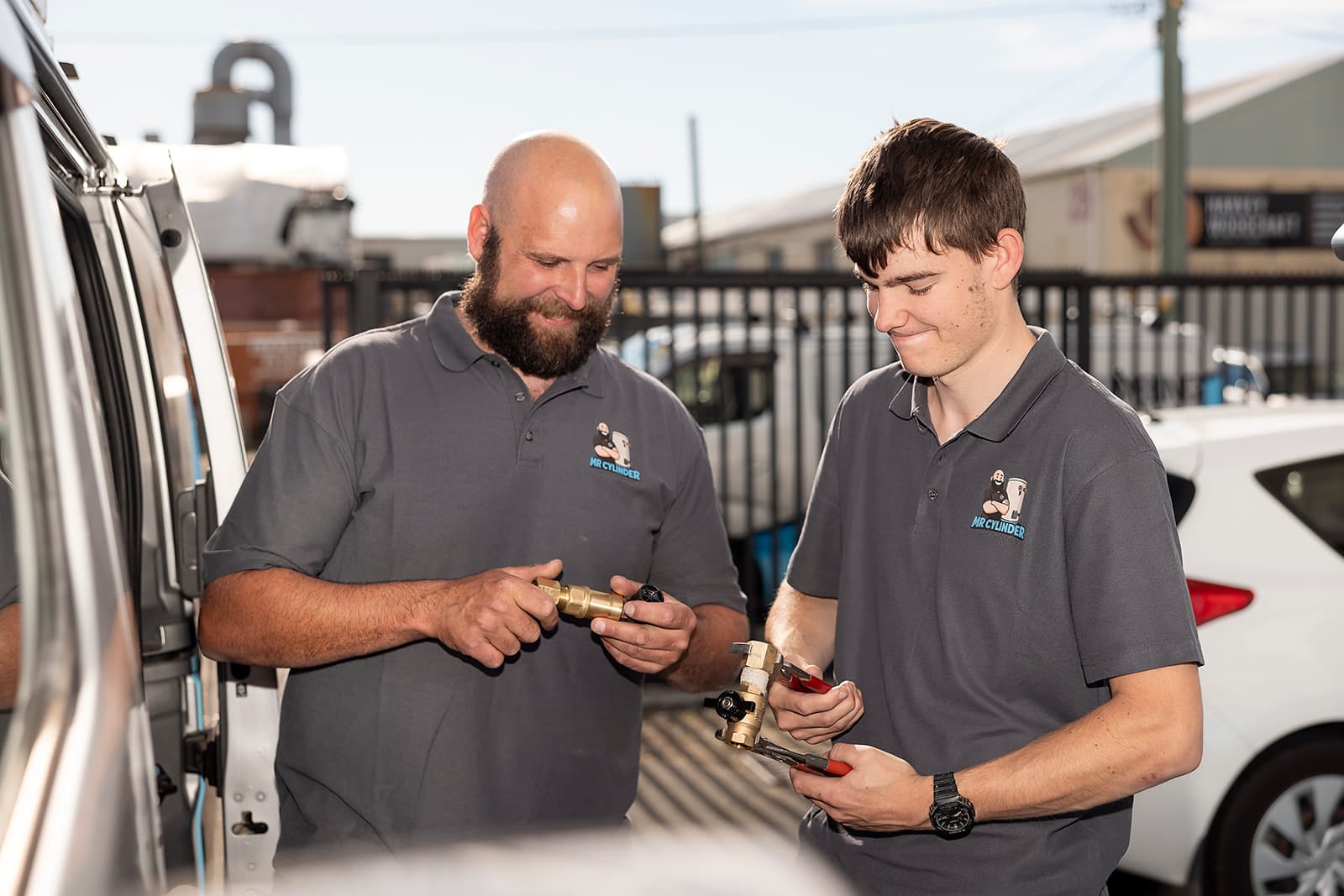 Two Mr Cylinder technicians examining plumbing fittings beside their van